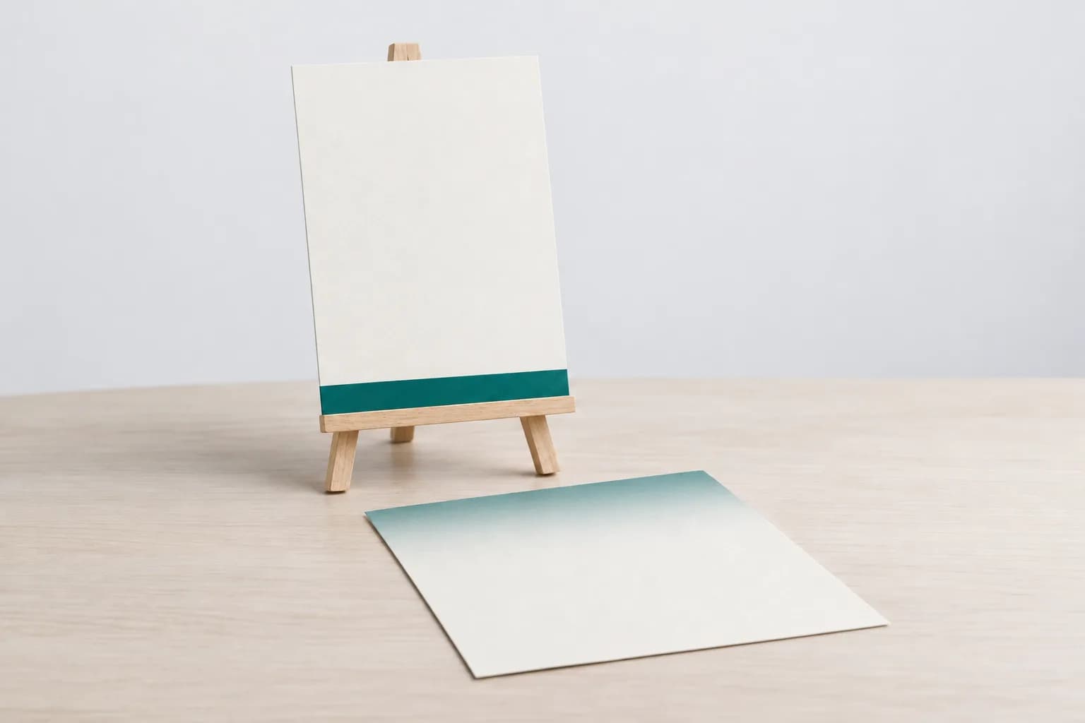 A small blank poster on a tabletop easel with a turquoise stripe along the bottom, next to a blank sheet of paper whose top third is shaded turquoise